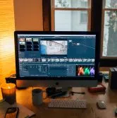 Bureau à domicile confortable de videaste mariage toulouse avec un ordinateur affichant des logiciels de montage vidéo, entouré de plantes et d'une décoration chaleureuse